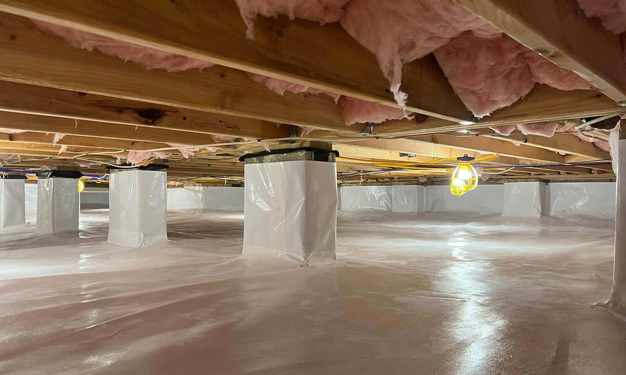crawl space under a home with white vapor barrier on floor and wrapped up piers