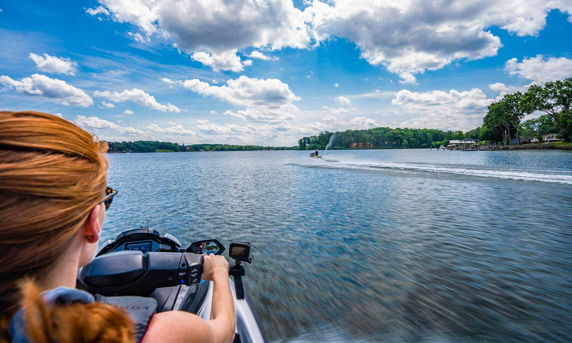 view from behind shoulder of red haired female driving a jet ski on a beautiful lake with blue skies